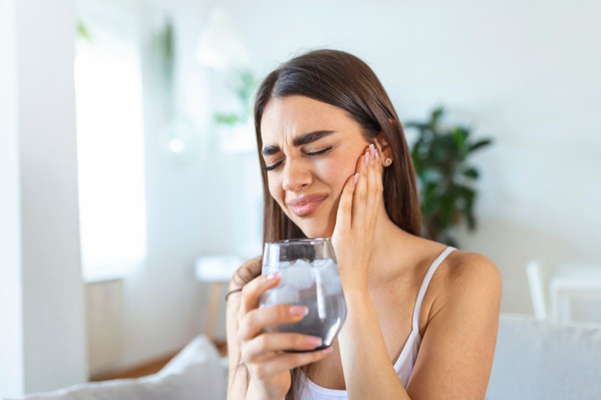Woman experiencing tooth sensitivity and pain after drinking ice water.