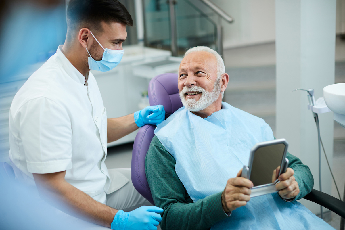 older adult man sitting in dental chair talking to dentist