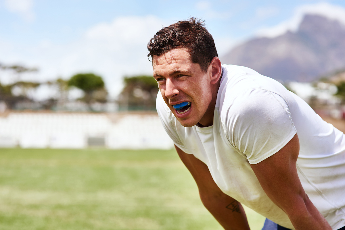 man on athletic field breathing heavily with blue mouthguard