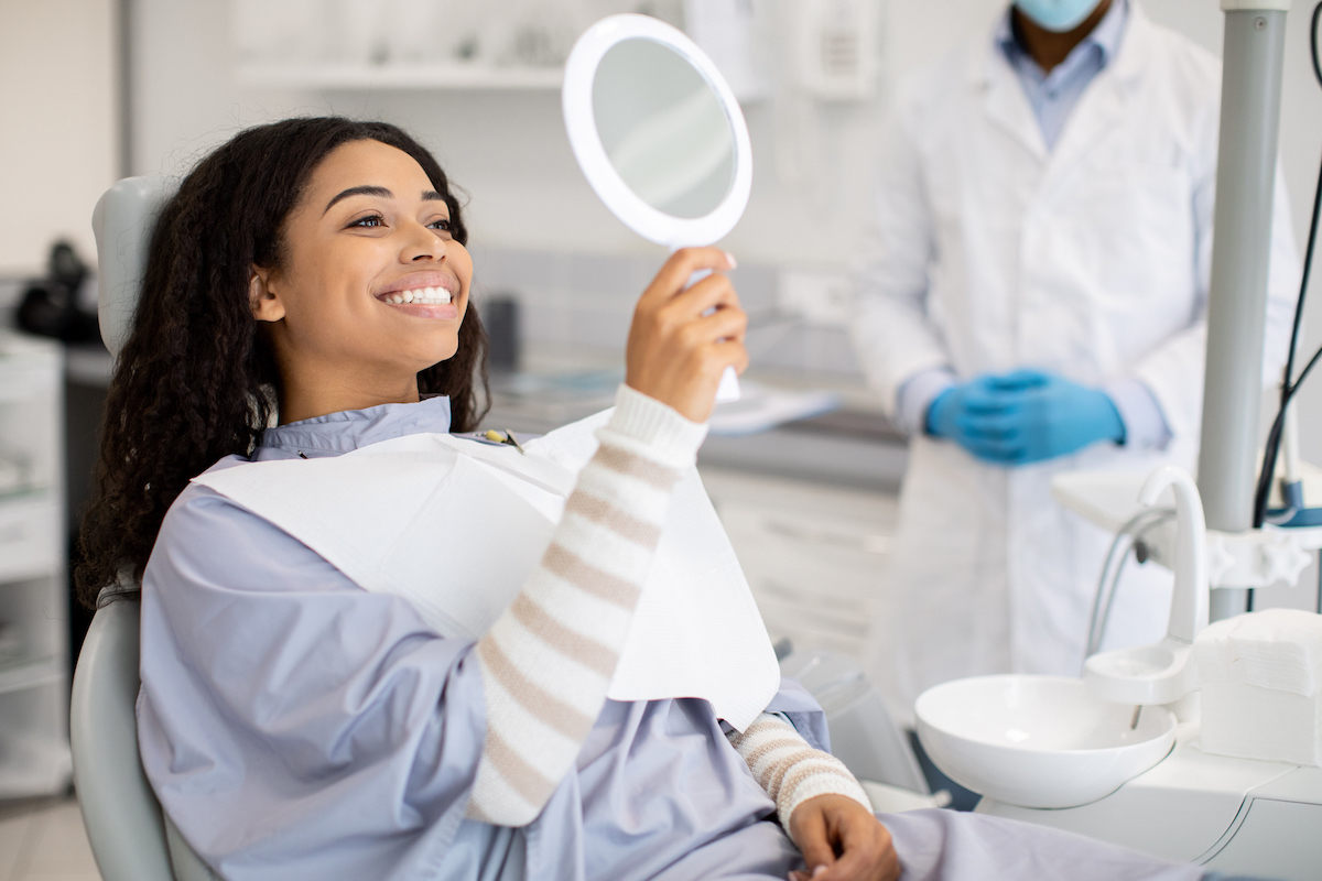 woman sitting in a dental chair admiring her smile in a mirror