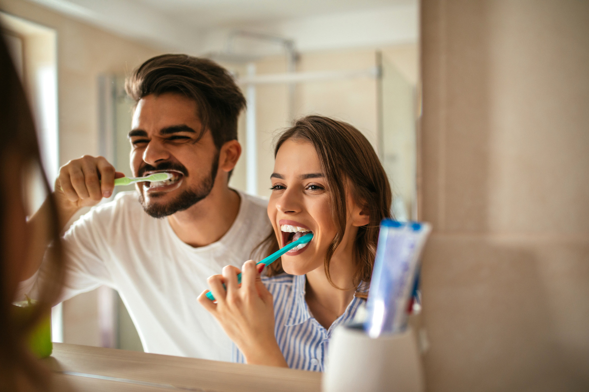 man and woman brushing teeth together in the mirror