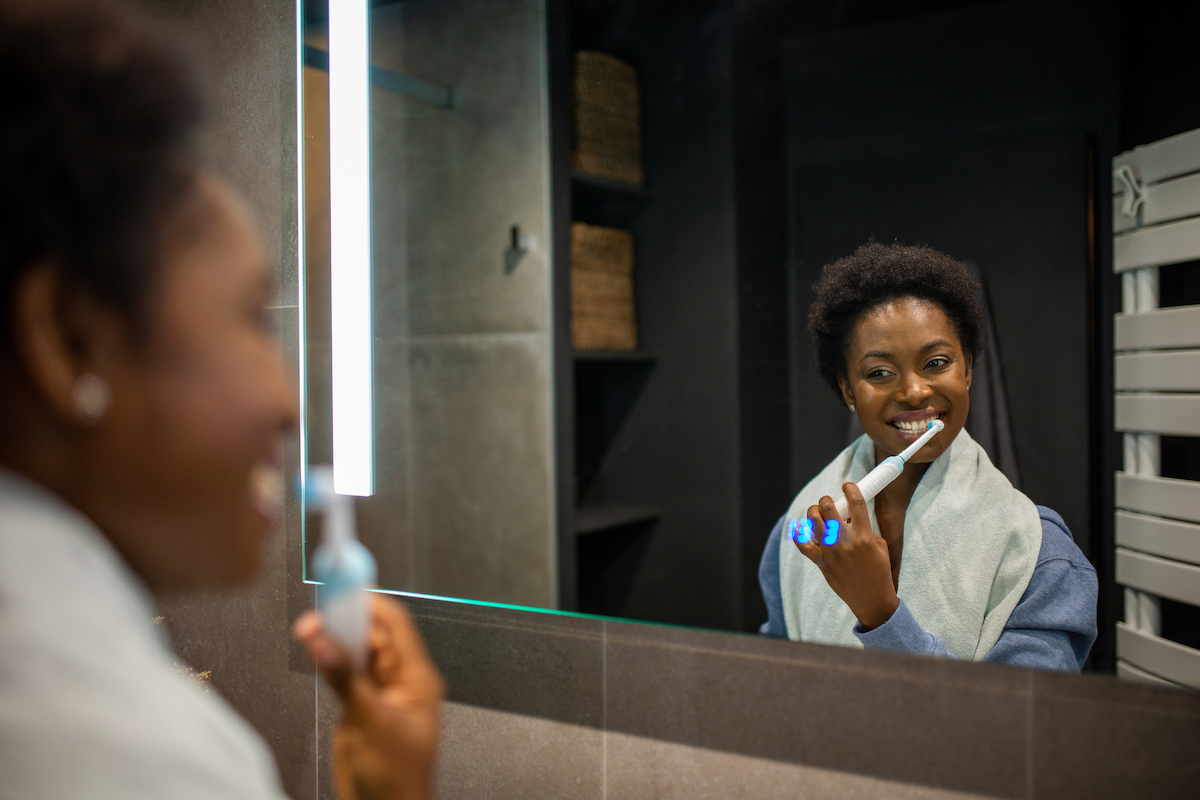 woman brushing teeth in the mirror with electric toothbrush
